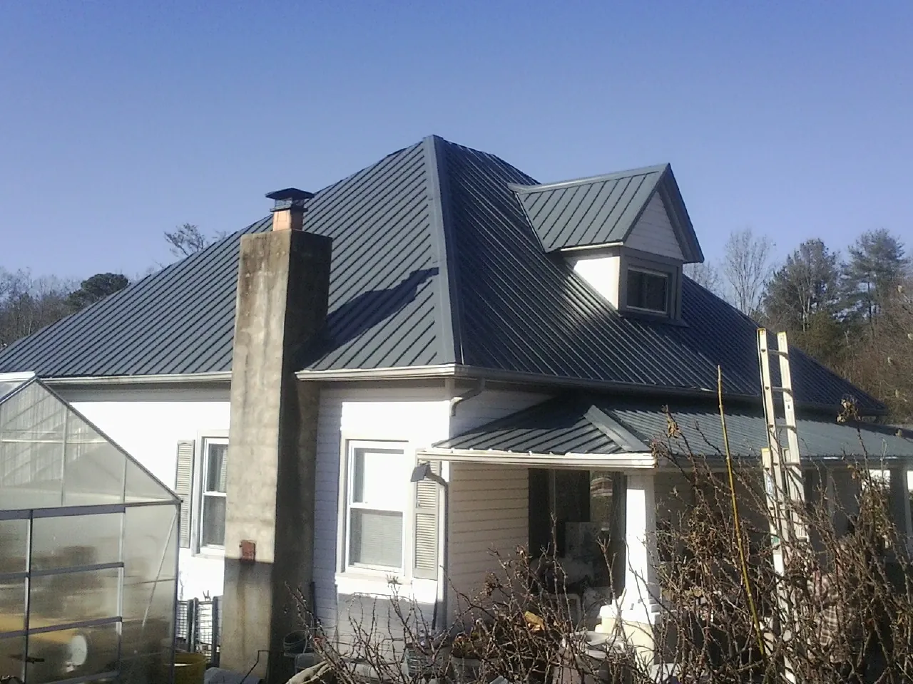Dark blue standing seam metal roof on a white farmhouse with dormer — Slate & Tile Roof Repair by Roofing Brothers in Longbranch