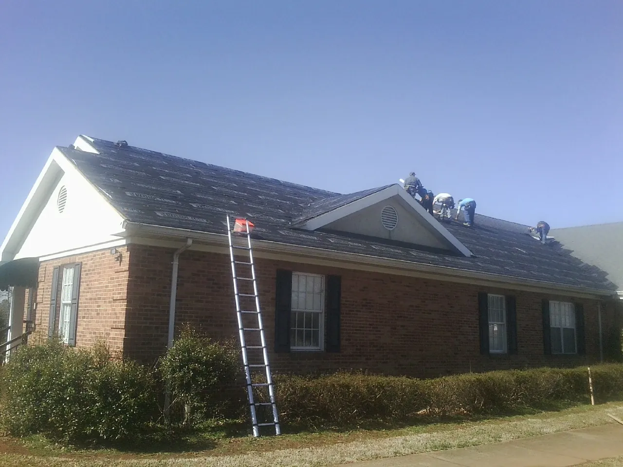 Crew tearing shingles off a brick ranch roof with a ladder set — Emergency Roof Repair work by our crew in Longbranch