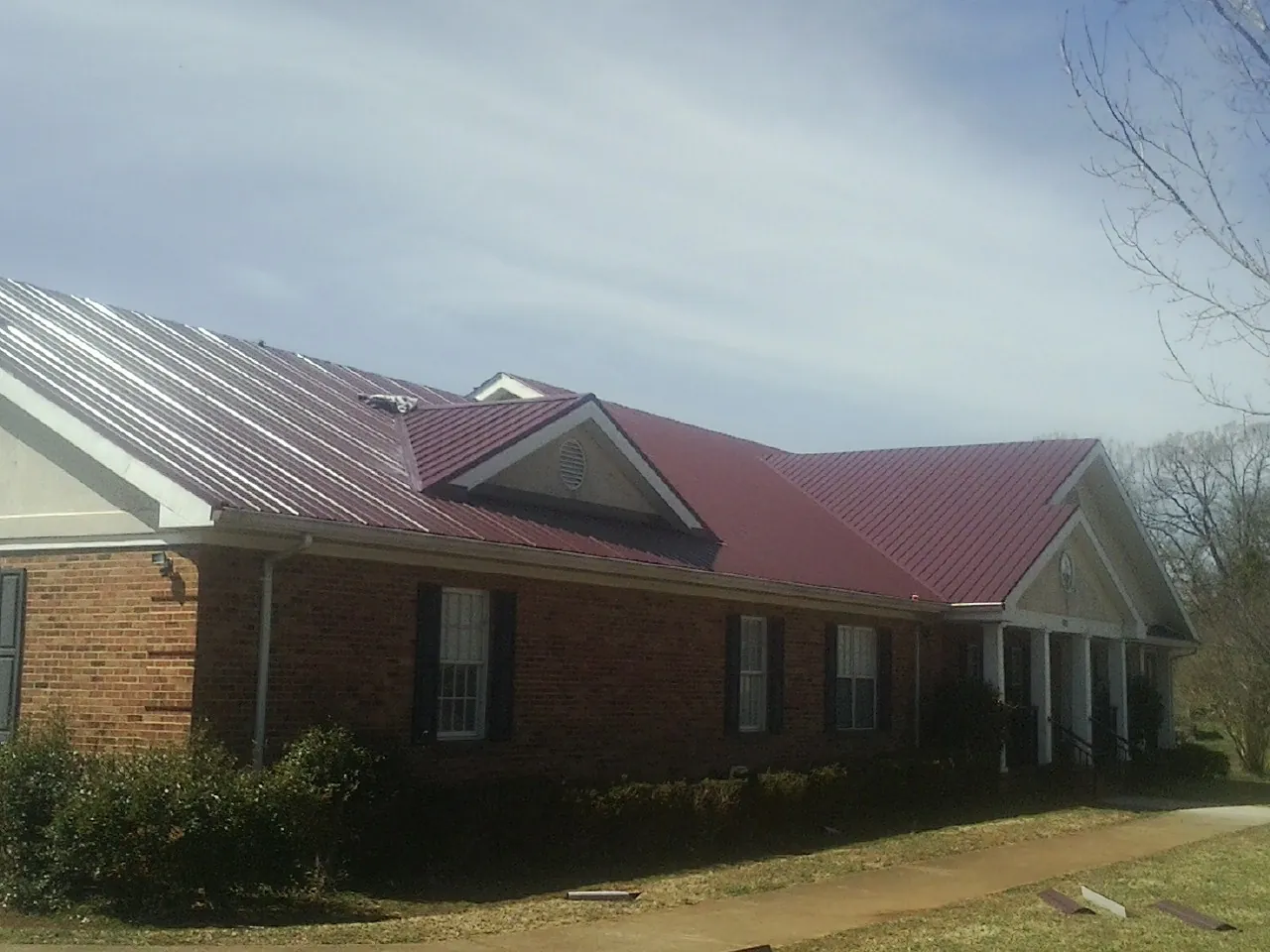 Red metal roof with gabled entries on a long brick building, from a Hail Damage Roof Repair job in Longbranch