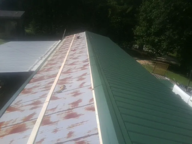 Old rusted panels beside newly installed green metal roofing — Wind Damage Roof Repair by Roofing Brothers in Longbranch