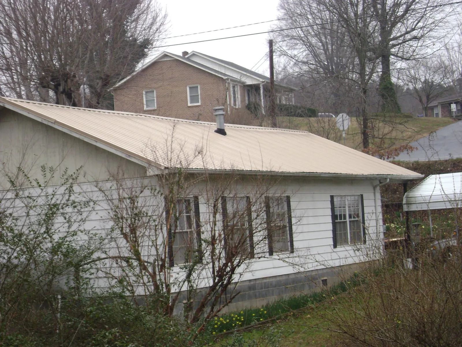 Tan metal roof on a white sided house set into a hillside — Commercial Roofing by Roofing Brothers in Longbranch