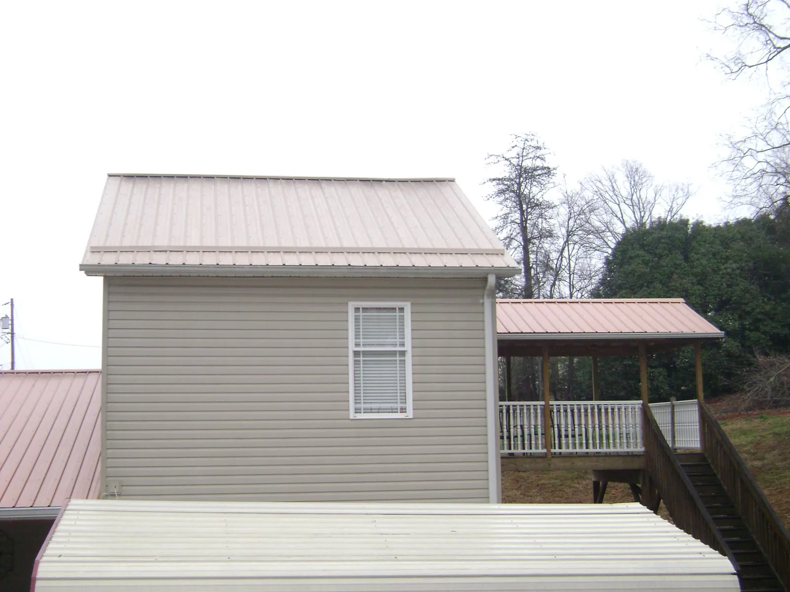 Tan metal roofs on a two story addition and attached porch, from a Roof Replacement job in Longbranch